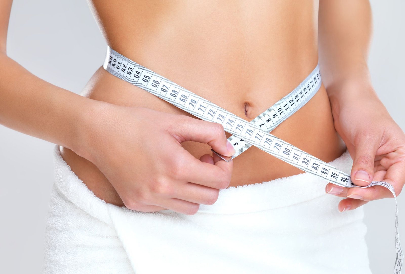 Woman measuring her waist with a tape measure for body contouring treatment.